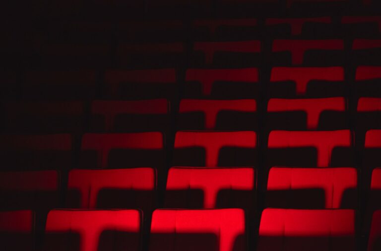 Dramatic spotlight illuminating an empty stage with deep red velvet theatre seats in a historic performance hall, evoking anticipation and a sense of classic nostalgia.